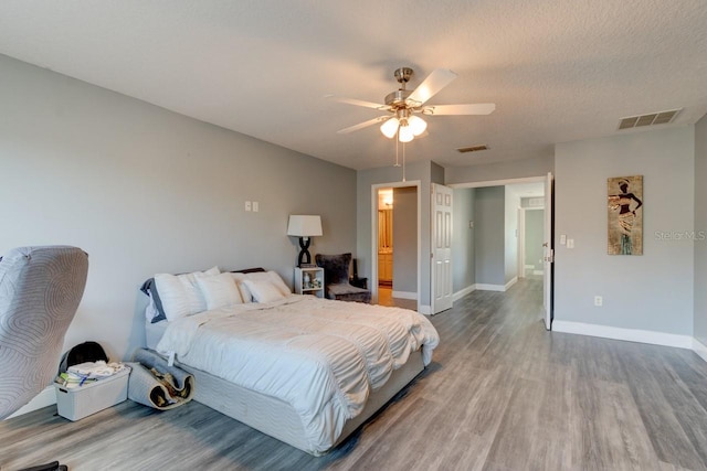 bedroom with a textured ceiling, hardwood / wood-style flooring, ensuite bath, and ceiling fan