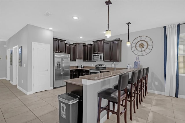 kitchen with kitchen peninsula, stainless steel appliances, pendant lighting, light tile patterned floors, and stone counters