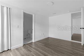 unfurnished bedroom with ensuite bathroom and dark wood-type flooring