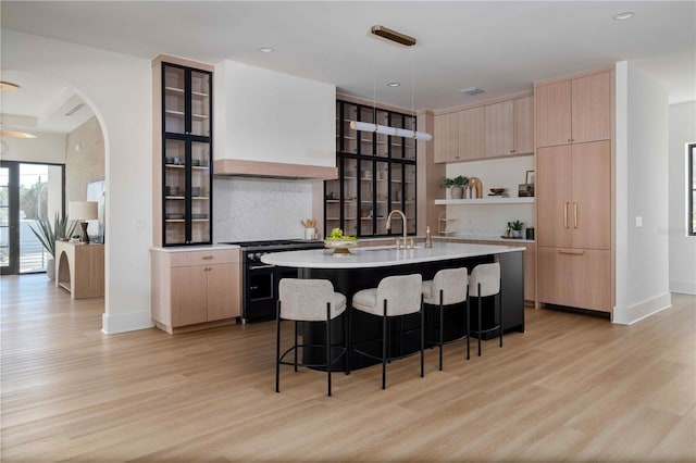 kitchen featuring sink, hanging light fixtures, light hardwood / wood-style flooring, a center island with sink, and stainless steel stove