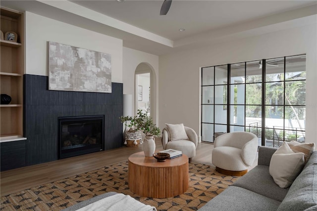 living room with a tile fireplace, built in shelves, hardwood / wood-style flooring, and ceiling fan