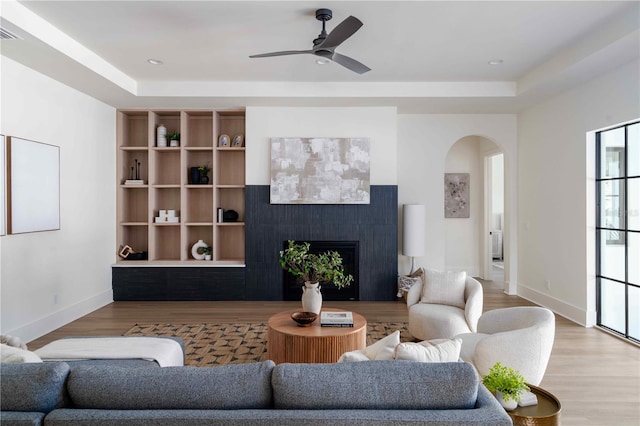 living room with light wood-type flooring, a tray ceiling, and ceiling fan