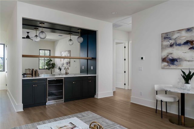 bar featuring pendant lighting, wood-type flooring, sink, and beverage cooler