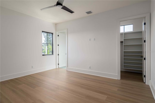 unfurnished bedroom featuring hardwood / wood-style floors, a closet, a spacious closet, and ceiling fan