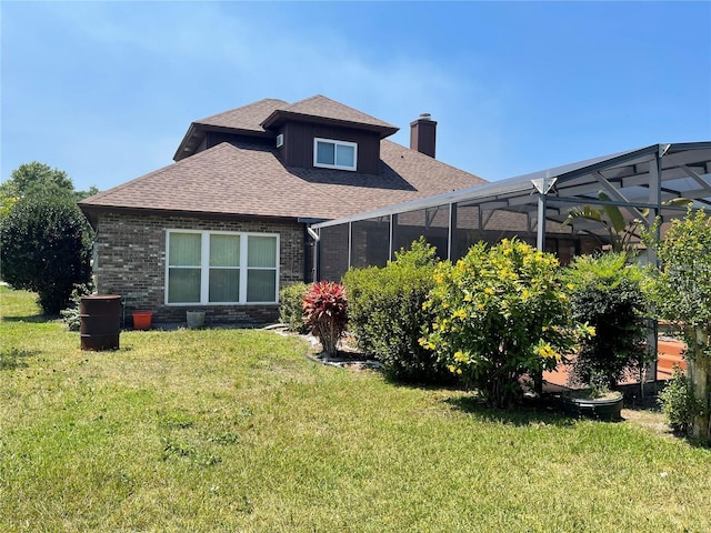 back of house with glass enclosure, roof with shingles, a chimney, a lawn, and brick siding