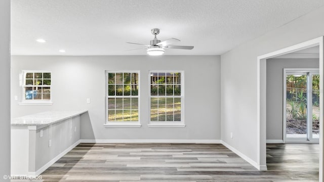 unfurnished dining area featuring a textured ceiling, light hardwood / wood-style floors, ceiling fan, and a healthy amount of sunlight