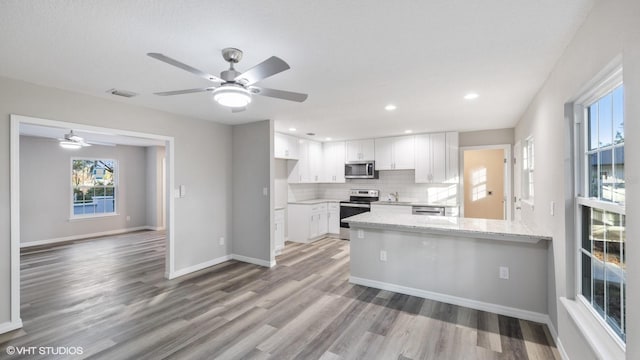 kitchen with light stone countertops, white cabinetry, stainless steel appliances, backsplash, and kitchen peninsula