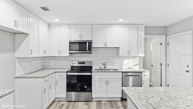 kitchen with backsplash, sink, light stone counters, white cabinetry, and stainless steel appliances