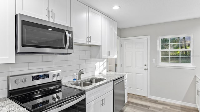 kitchen with white cabinets, stainless steel appliances, light stone countertops, and sink