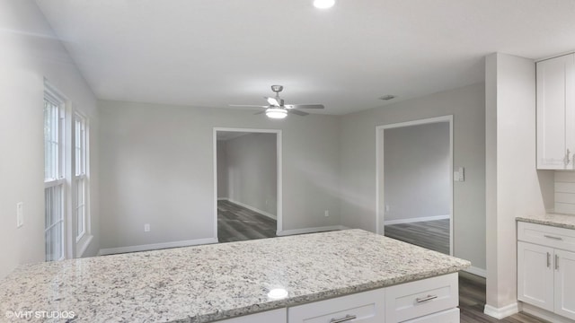 kitchen featuring white cabinets, ceiling fan, light stone countertops, and dark wood-type flooring