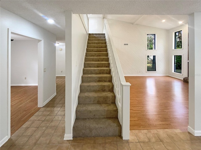 stairway featuring lofted ceiling, wood-type flooring, and a textured ceiling