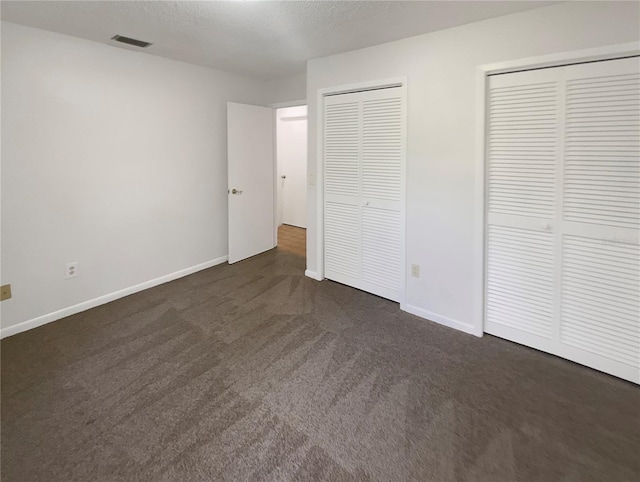 unfurnished bedroom featuring multiple closets and dark colored carpet