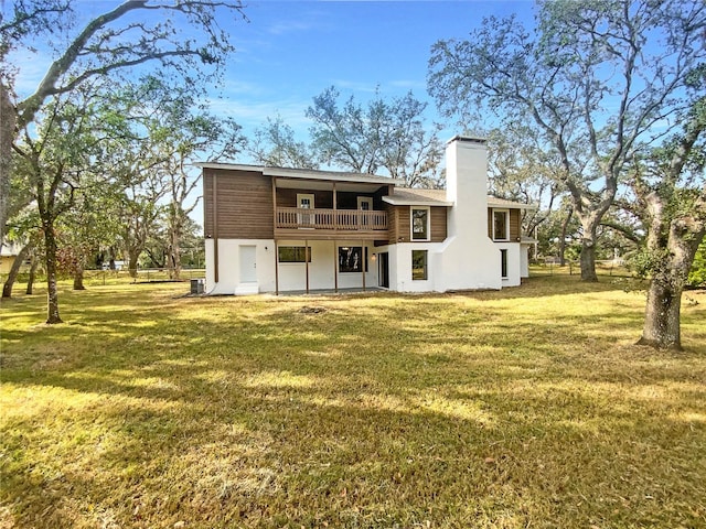 rear view of property featuring central air condition unit, a balcony, and a lawn