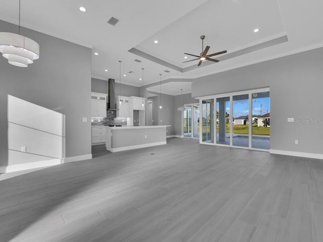 unfurnished living room with a raised ceiling, ceiling fan, and light hardwood / wood-style flooring