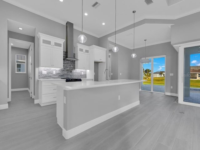 kitchen with white cabinets, pendant lighting, wall chimney range hood, and a kitchen island with sink