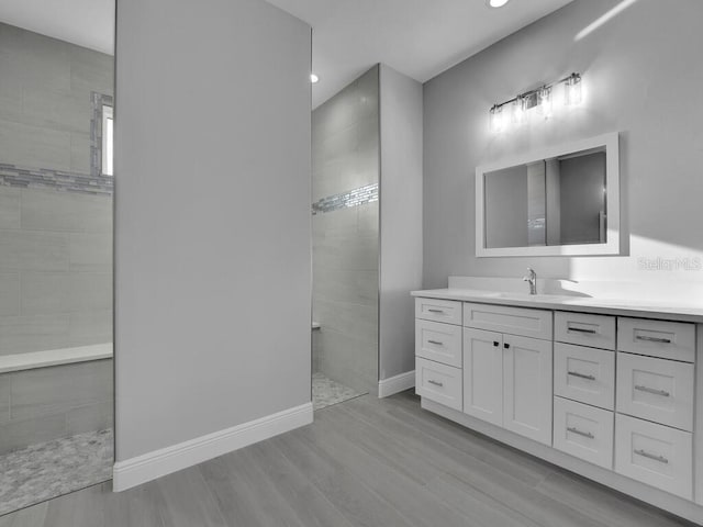 bathroom with hardwood / wood-style floors, vanity, and a tile shower