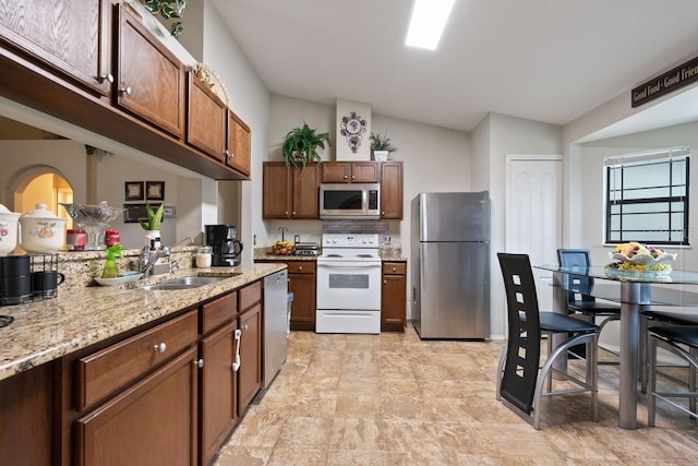 kitchen with light stone countertops, sink, stainless steel appliances, and vaulted ceiling