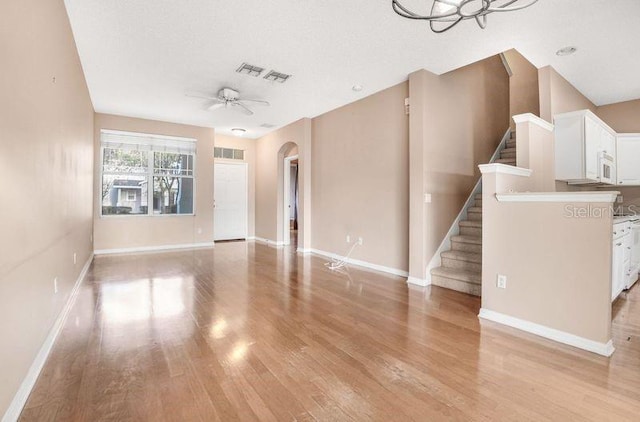 unfurnished living room with a textured ceiling, ceiling fan with notable chandelier, and light hardwood / wood-style floors