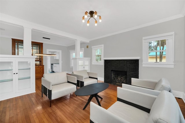 living room featuring a chandelier, wood-type flooring, a brick fireplace, and crown molding