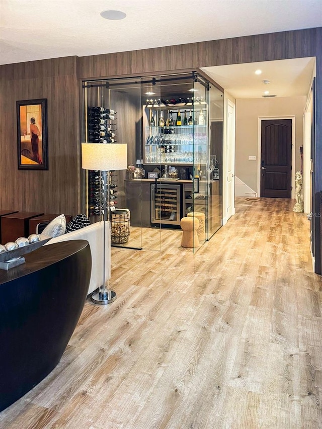 wine area with wooden walls, beverage cooler, light hardwood / wood-style floors, and indoor bar