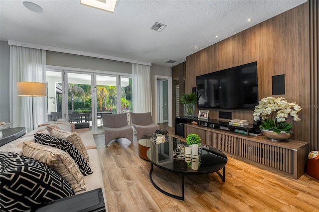 living room featuring wooden walls, light hardwood / wood-style flooring, and a textured ceiling