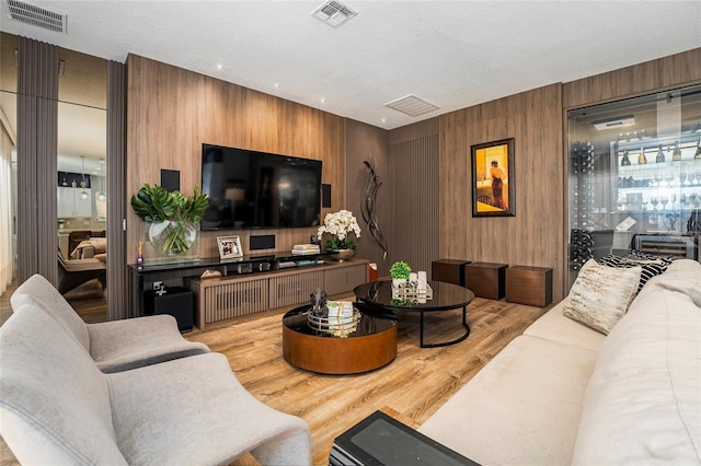 living room featuring a textured ceiling, light hardwood / wood-style floors, and wood walls