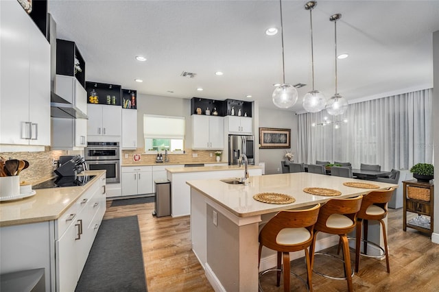 kitchen featuring pendant lighting, a kitchen island with sink, light stone countertops, appliances with stainless steel finishes, and a kitchen bar