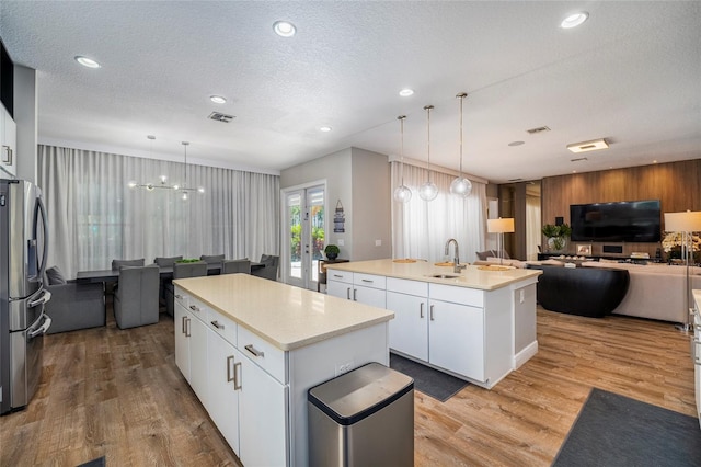 kitchen with stainless steel refrigerator with ice dispenser, light wood-type flooring, a textured ceiling, white cabinets, and an island with sink