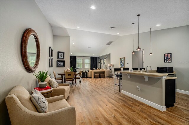 interior space featuring sink, lofted ceiling, a textured ceiling, and light hardwood / wood-style flooring