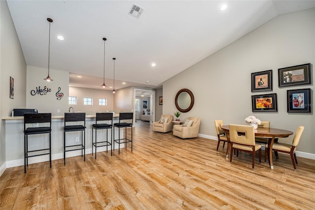 kitchen with decorative light fixtures, lofted ceiling, a breakfast bar area, and light hardwood / wood-style flooring