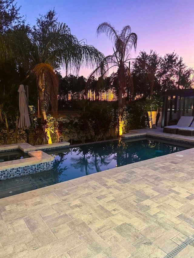 pool at dusk featuring a patio area and an in ground hot tub