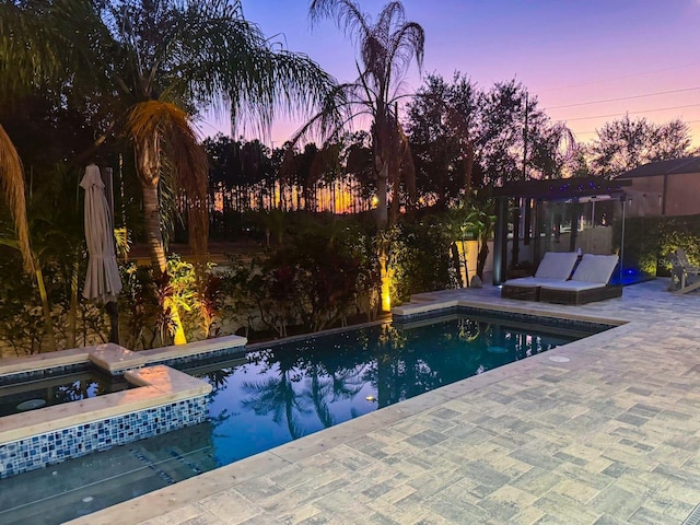 pool at dusk featuring an in ground hot tub and a patio