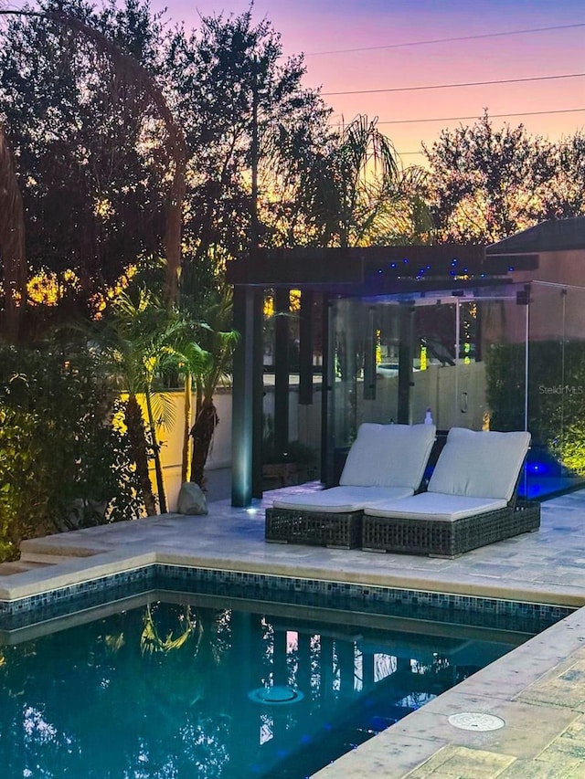 pool at dusk with a patio area