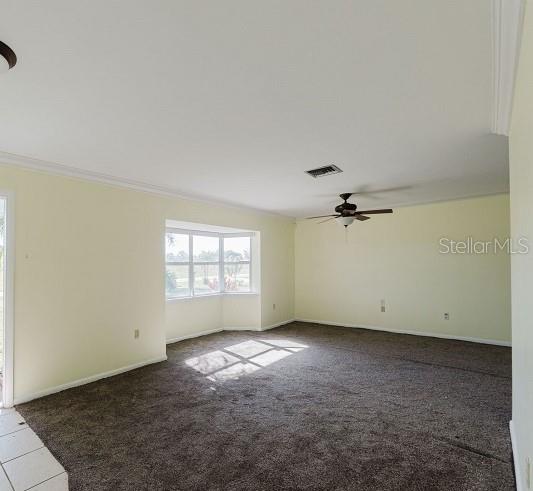 unfurnished room with dark colored carpet, ceiling fan, and ornamental molding