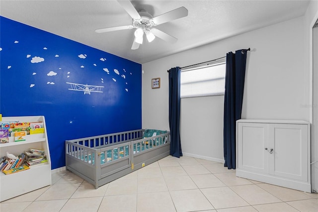 tiled bedroom with ceiling fan, a nursery area, and a textured ceiling