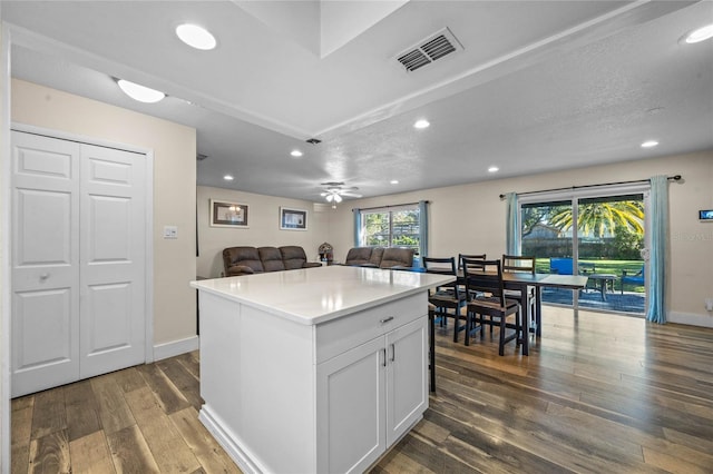 kitchen with ceiling fan, dark hardwood / wood-style floors, a textured ceiling, a kitchen island, and white cabinetry