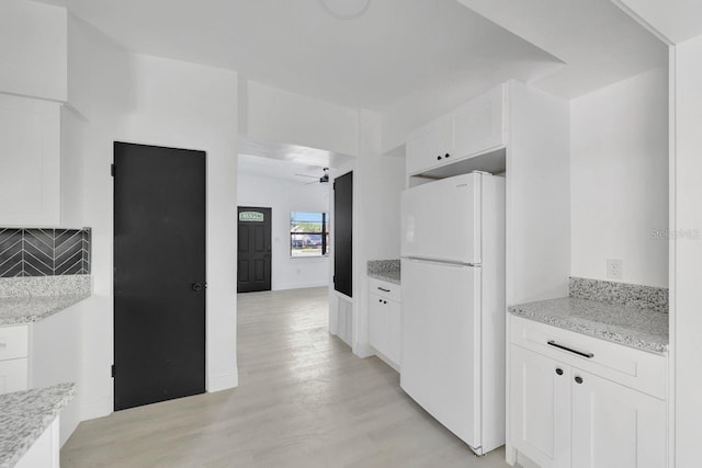 kitchen with white cabinets, light hardwood / wood-style flooring, decorative backsplash, light stone countertops, and white fridge