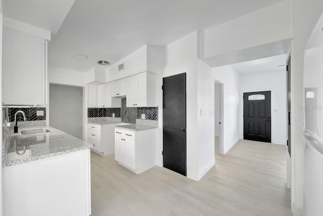 kitchen with light stone countertops, backsplash, sink, light hardwood / wood-style flooring, and white cabinets