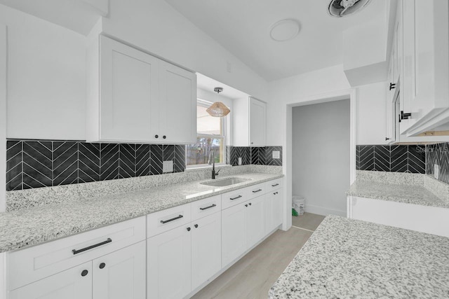 kitchen featuring backsplash, light stone countertops, white cabinetry, and sink