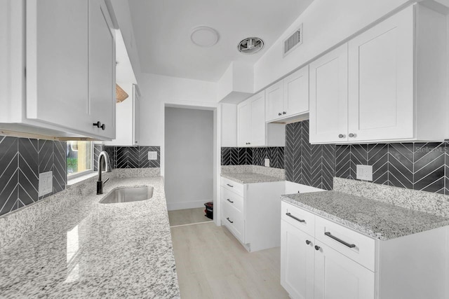 kitchen featuring light wood-type flooring, backsplash, white cabinetry, and sink