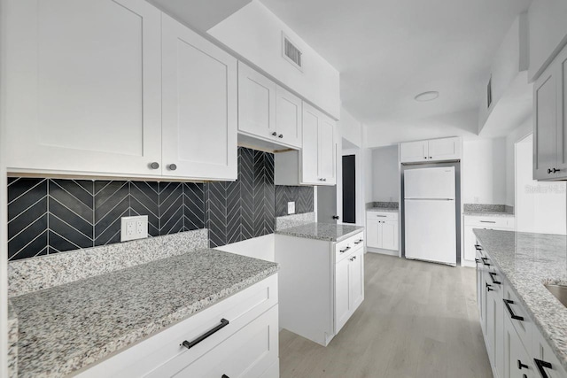 kitchen featuring decorative backsplash, light stone counters, white refrigerator, light hardwood / wood-style flooring, and white cabinetry