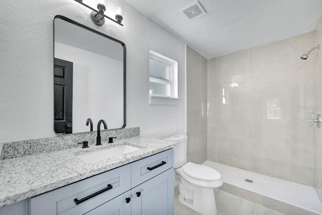 bathroom featuring vanity, a textured ceiling, tiled shower, and toilet