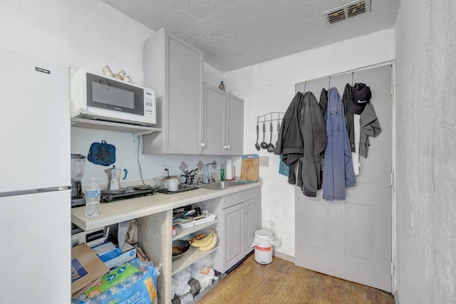 kitchen featuring a textured ceiling, light hardwood / wood-style flooring, white appliances, and sink