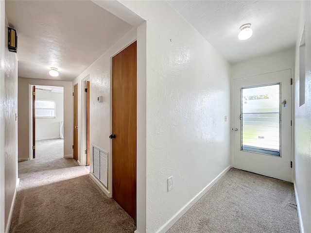 corridor with light colored carpet and a textured ceiling