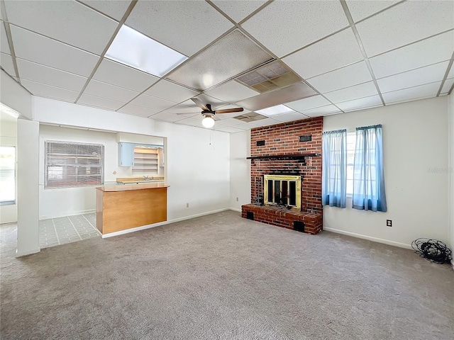 unfurnished living room featuring carpet, a paneled ceiling, a brick fireplace, and ceiling fan