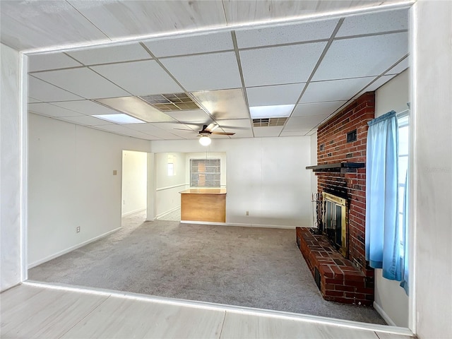 unfurnished living room with carpet flooring, ceiling fan, a drop ceiling, and a brick fireplace