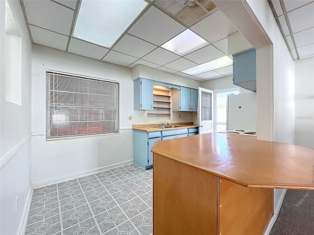 kitchen with a drop ceiling, white refrigerator, blue cabinets, sink, and butcher block countertops