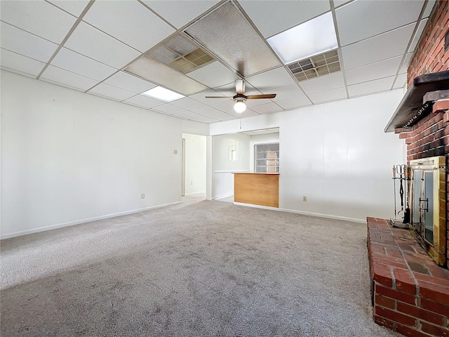 unfurnished living room with carpet flooring, ceiling fan, a drop ceiling, and a brick fireplace