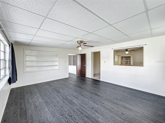 unfurnished room featuring built in shelves, a drop ceiling, and dark wood-type flooring