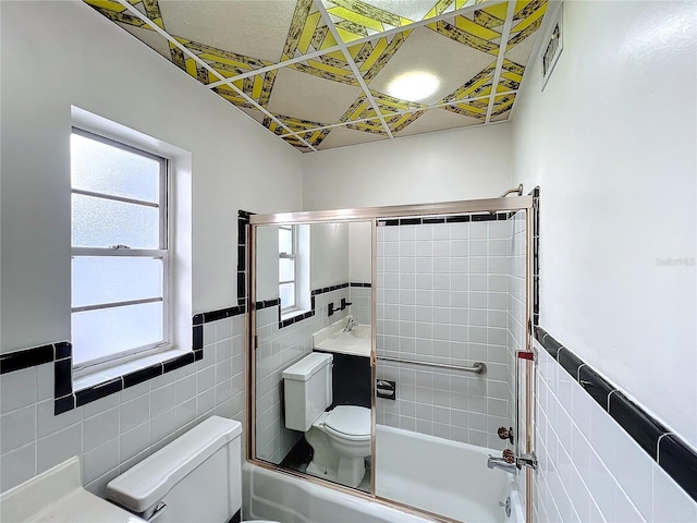 full bathroom featuring shower / bath combination with glass door, vanity, toilet, and tile walls